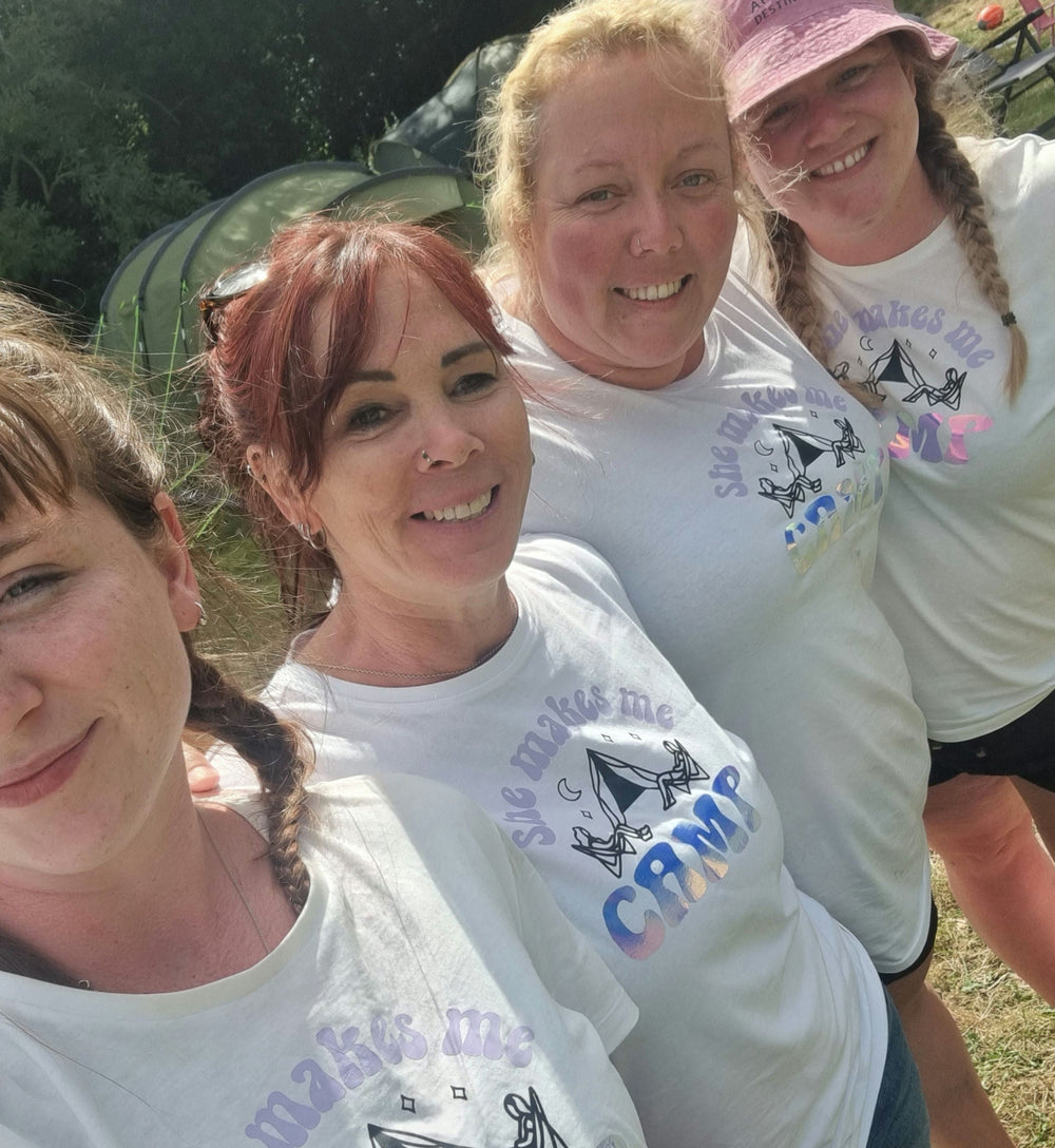 Four women wearing matching t-shirts with graphics and text, standing outdoors.