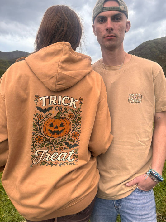 Caramel Latte coloured Halloween hoodie with a “Trick or Treat” pumpkin jack-o’-lantern design on the back surrounded by bats and autumn florals, and a smaller matching logo on the front chest. Made from organic fabric and sustainably crafted, this cute Halloween hoodie is nature-inspired with a festive pumpkin design. Couple models, modeling in the Lake District in Autumn. 