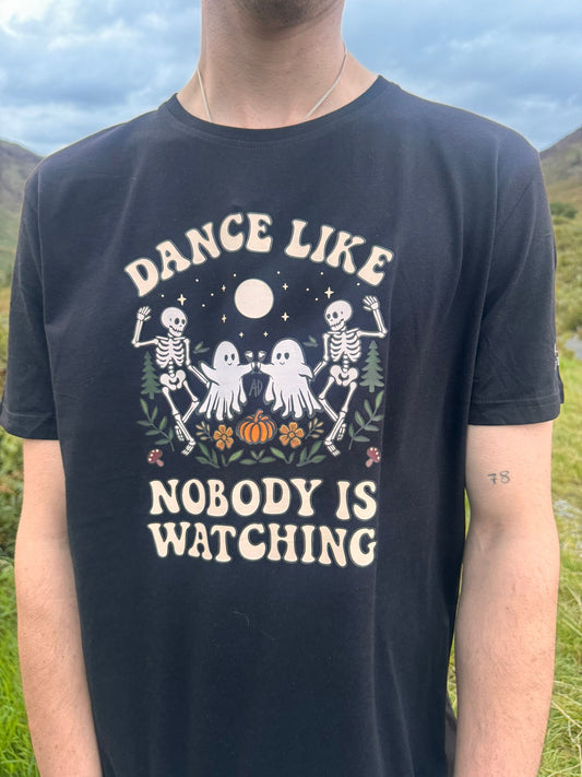 Organic black t-shirt, featuring ghosts and skeletons dancing on a bed of ferns pumpkins, sunflowers and conifers. Underneath the stars and moon. The writing boardering the design is a vintage retro font.